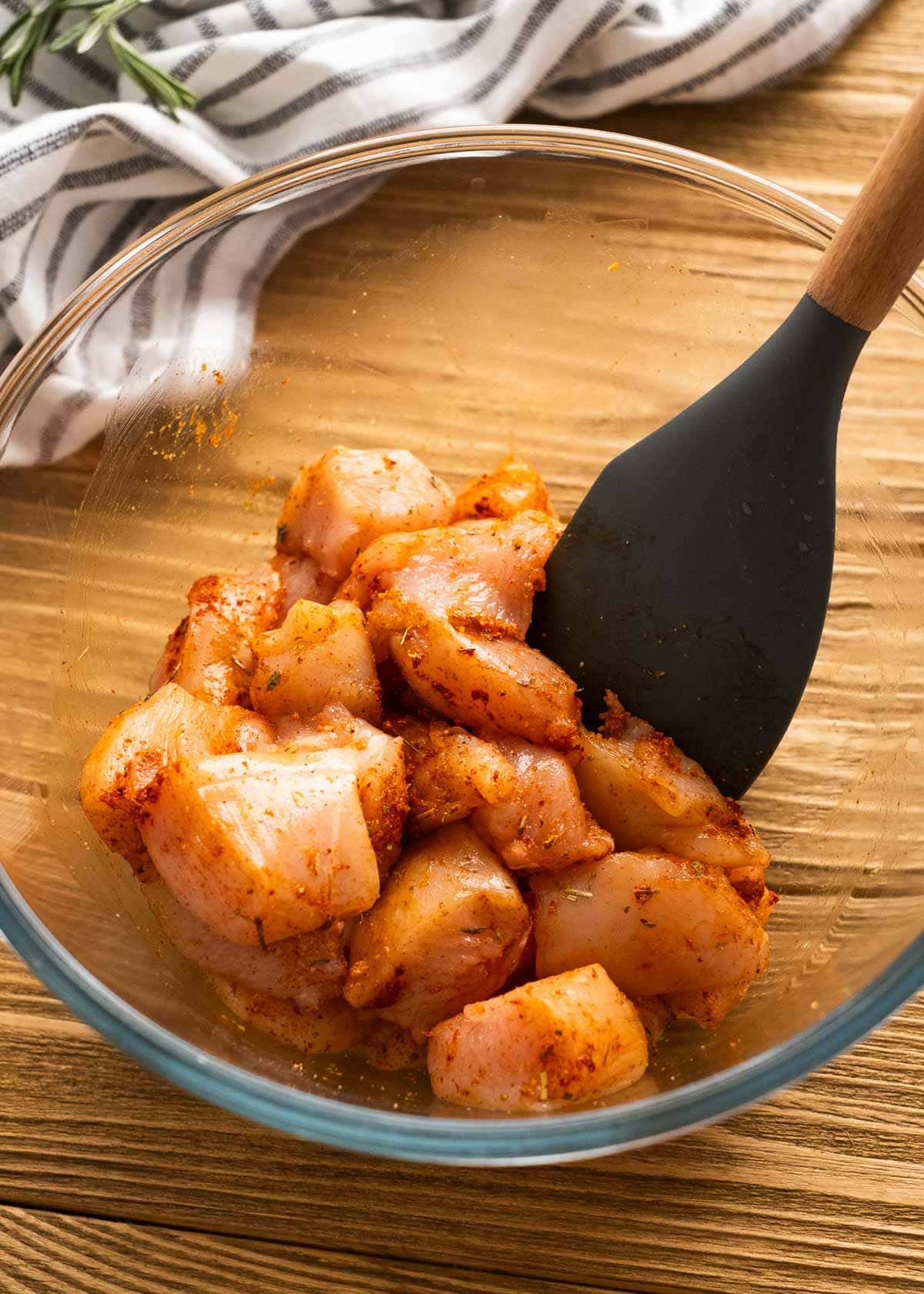 chicken bites being seasoned in a clear mixing bowl