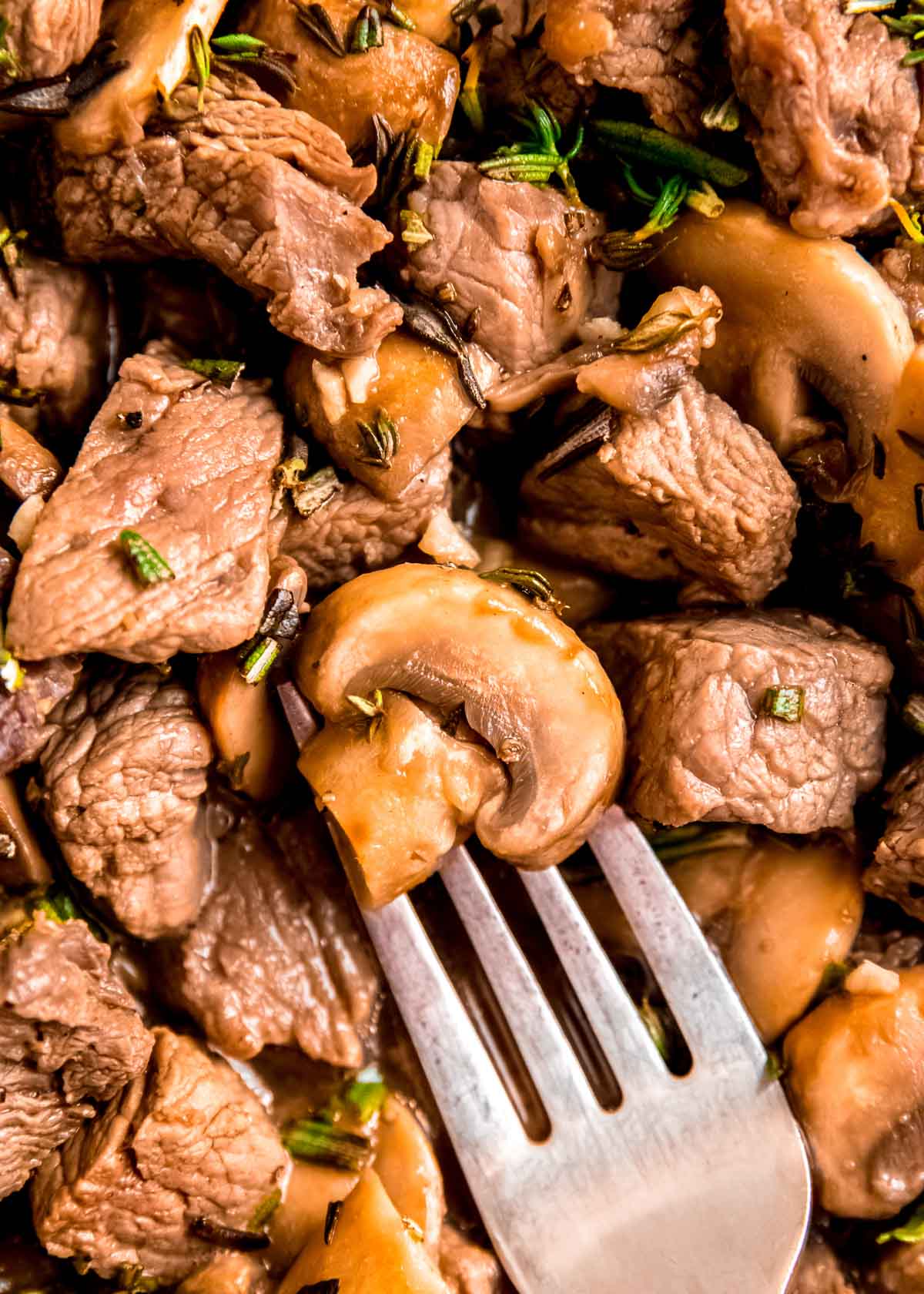 a fork with the perfect sauteed mushroom in a steak skillet