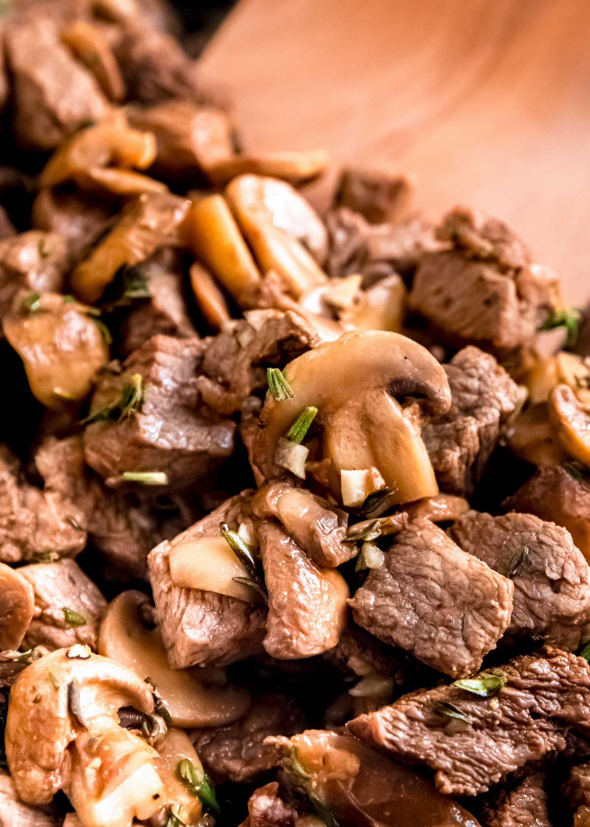 closeup of mushroom and steak bites garnished with fresh rosemary and thyme