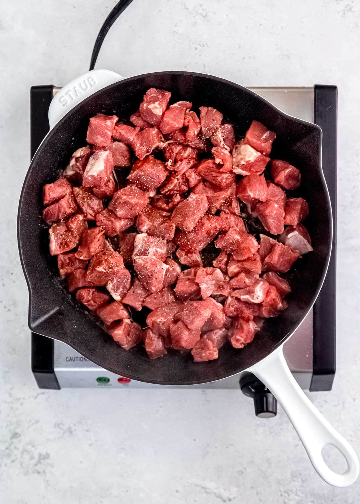 salt and pepper seasoning on steak tips in a skillet