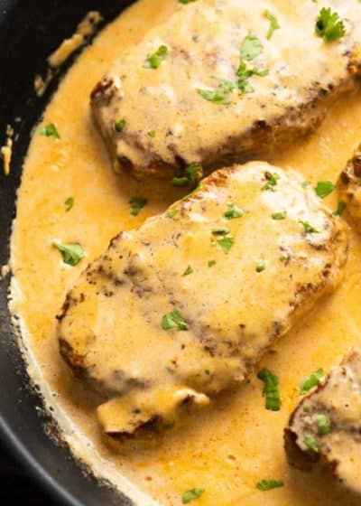 a large skillet with four juicy pork chops covered in a creamy Cajun sauce