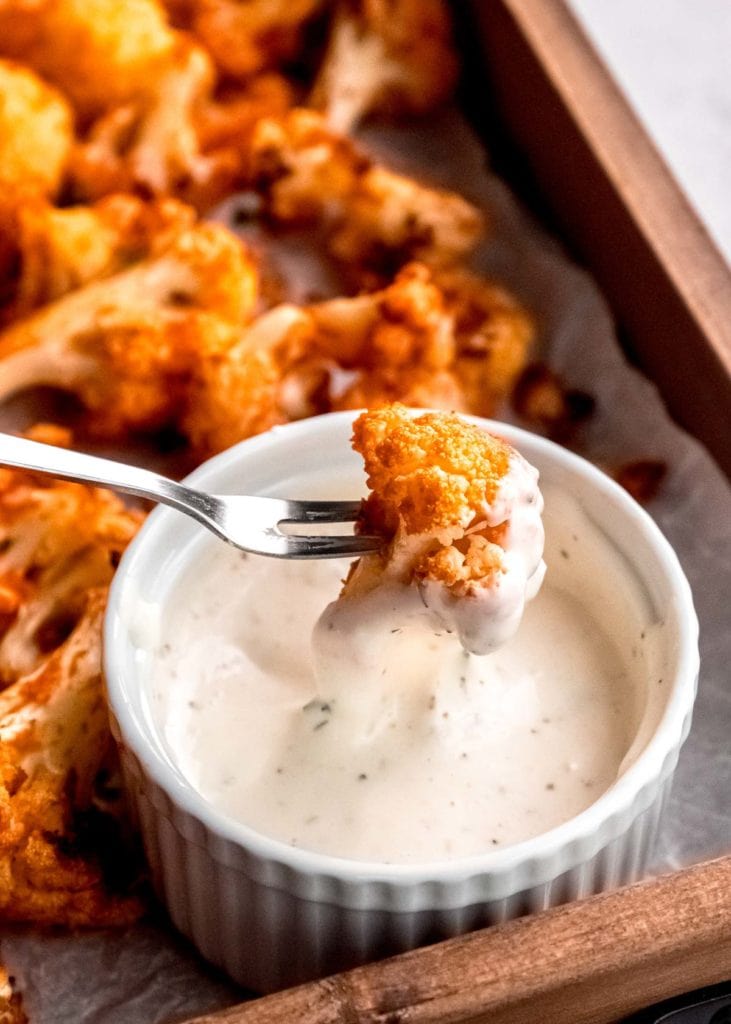 a fork dunking a piece of buffalo cauliflower into a ramekin with ranch or blue cheese dressing