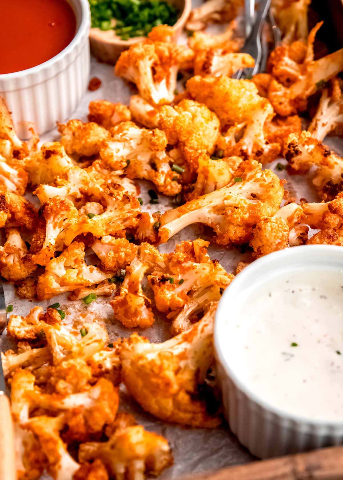 a side view of roasted buffalo cauliflower on a pan with ramekins with buffalo sauce and blue cheese dressing