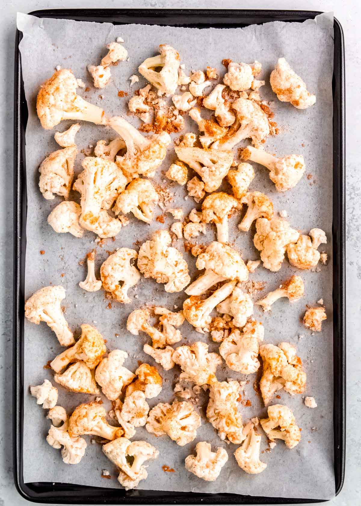 overhead image of seasoned cauliflower spread on a baking sheet