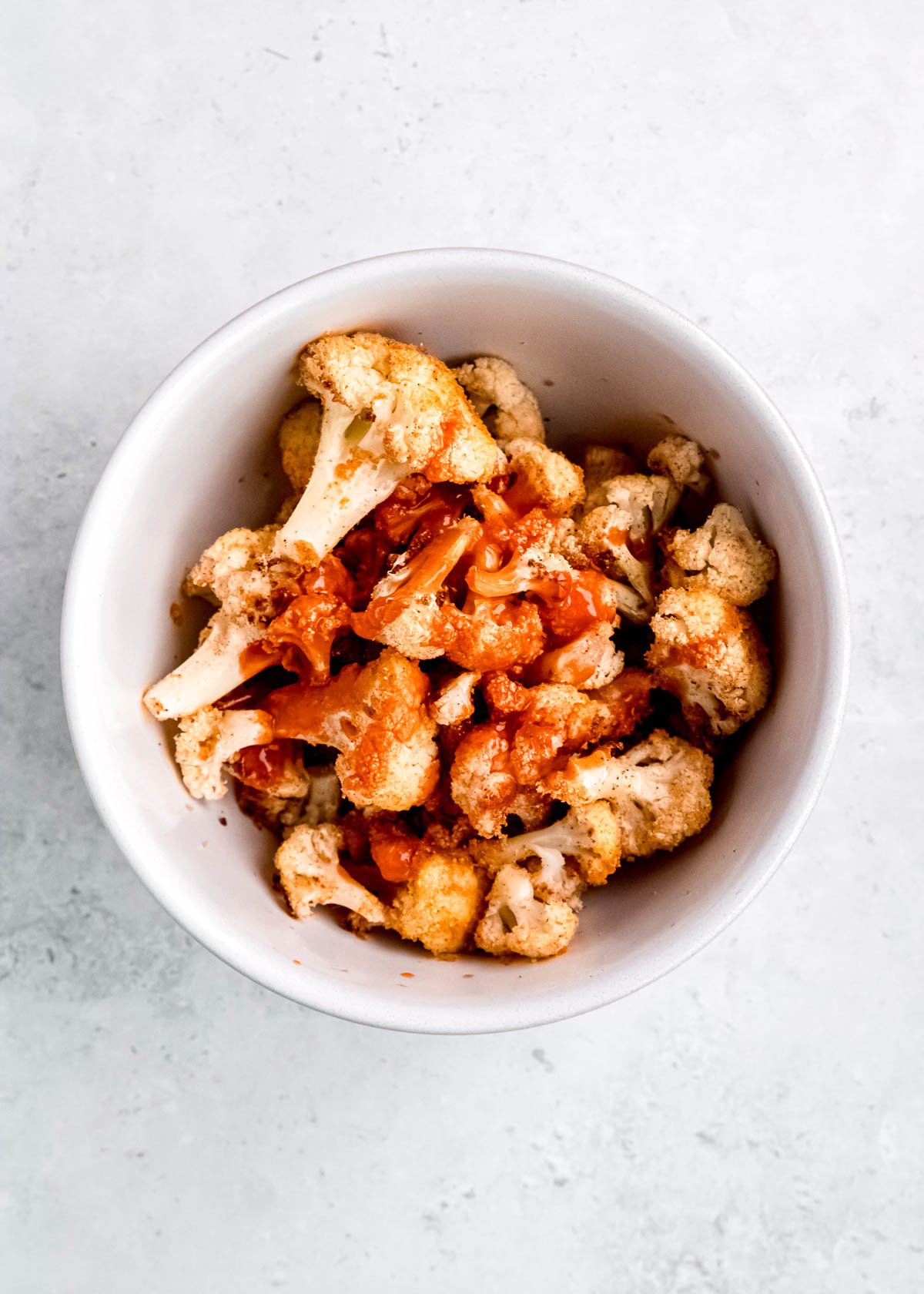 cauliflower being tossed in a white bowl with buffalo sauce