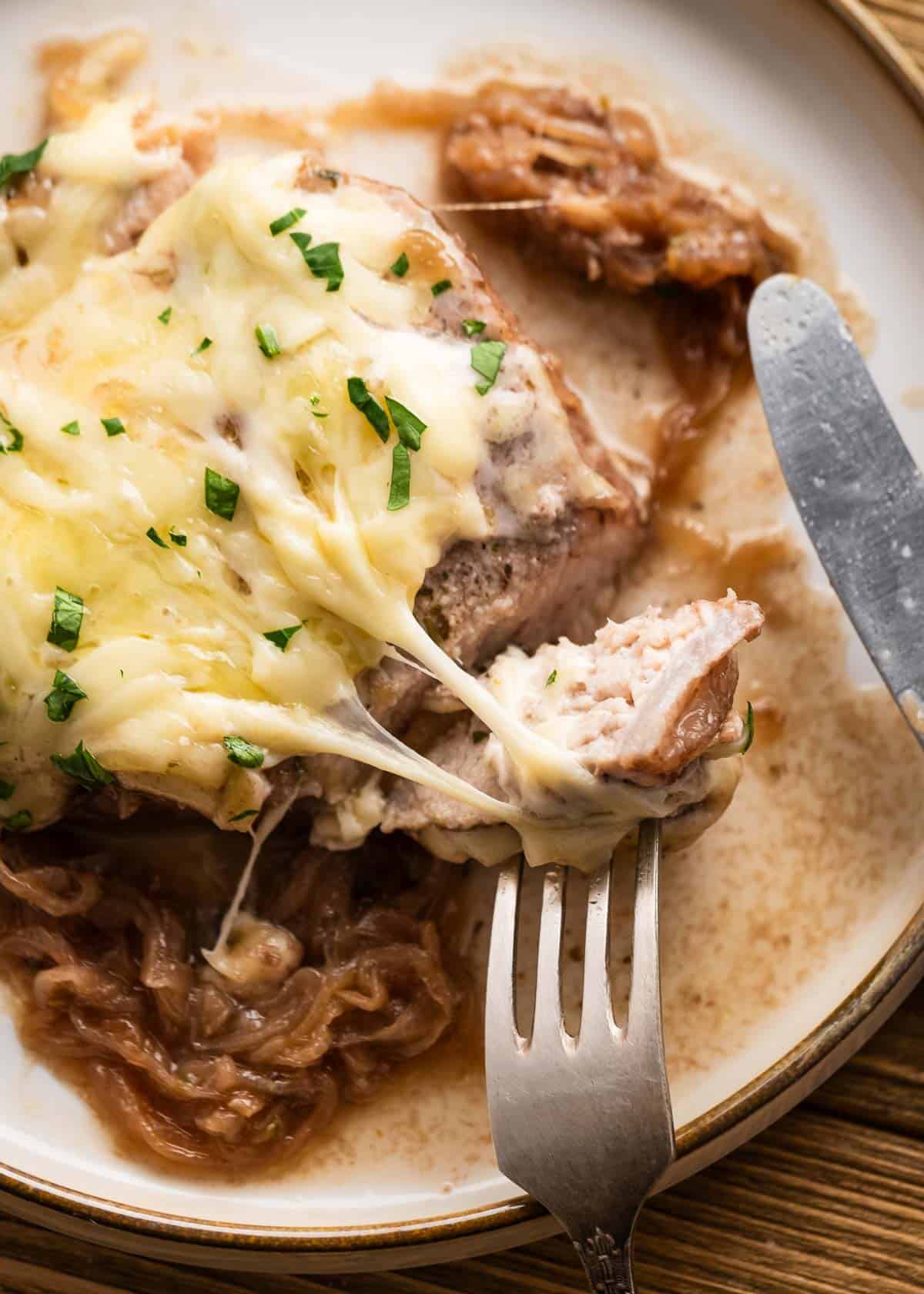 close up image of french onion pork chop and fork on white plate