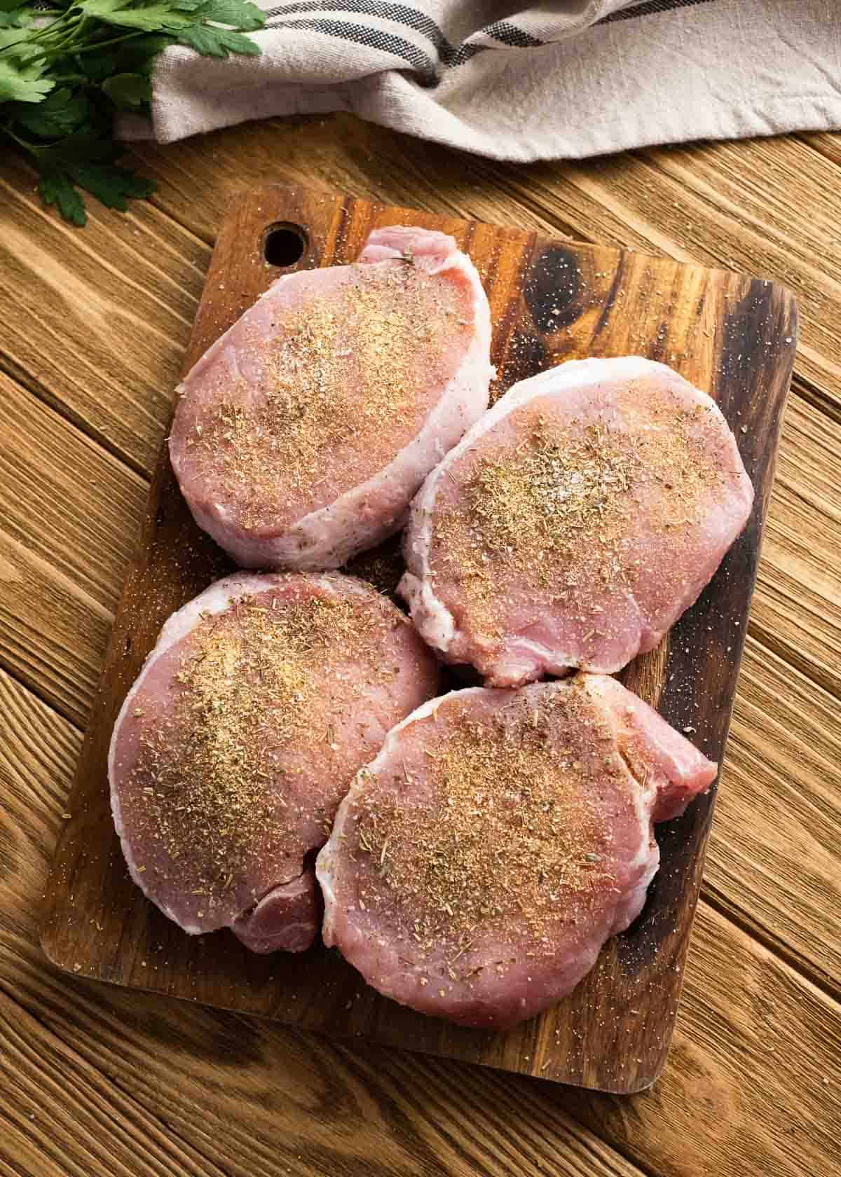 seasoned pork chops on a wooden cutting board