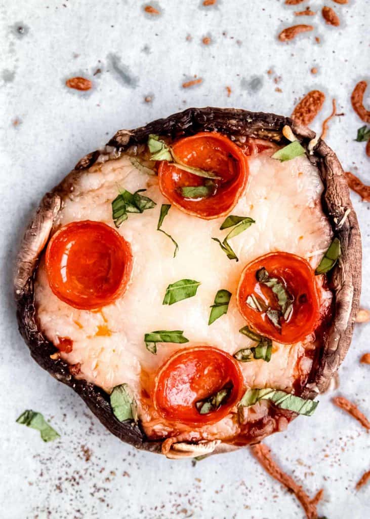 overhead shot of pepperoni pizza stuffed mushrooms finished with chopped basil on a piece of parchment paper