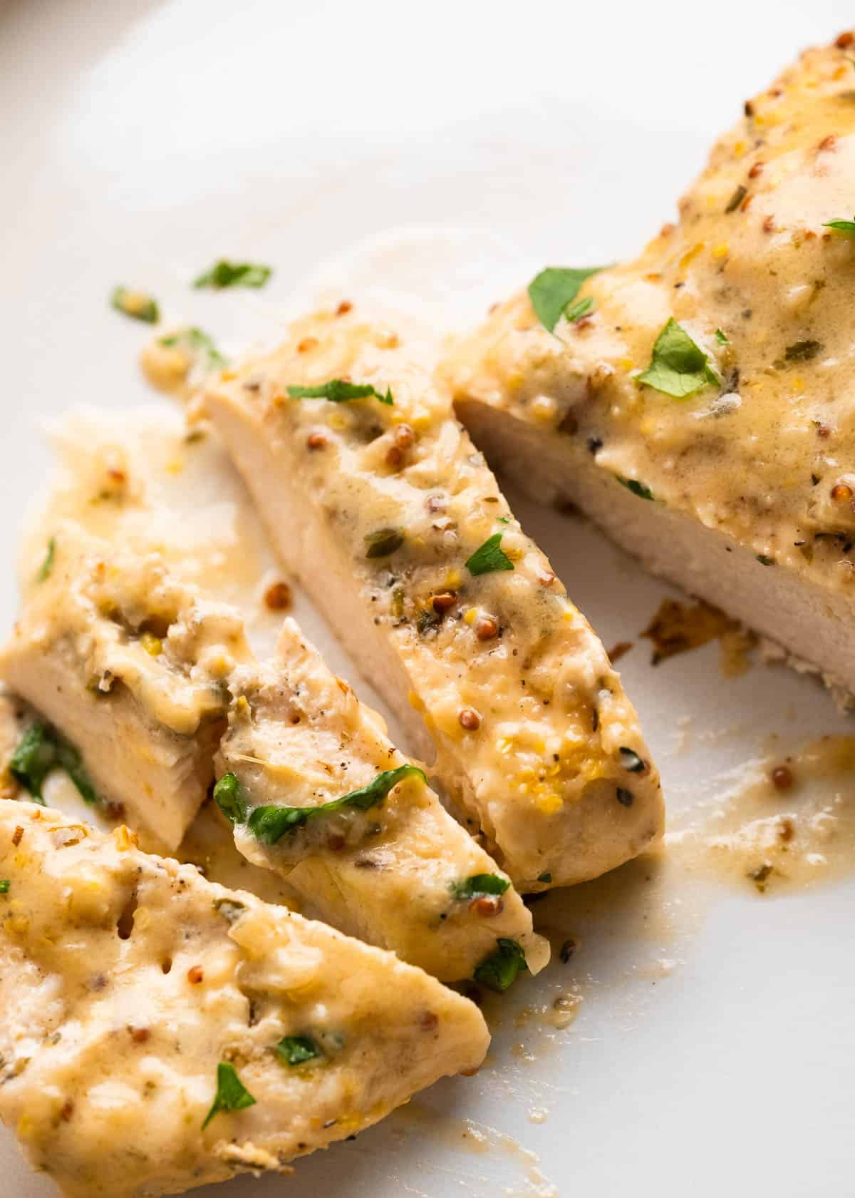 sliced chicken in mustard cream sauce on white cutting board