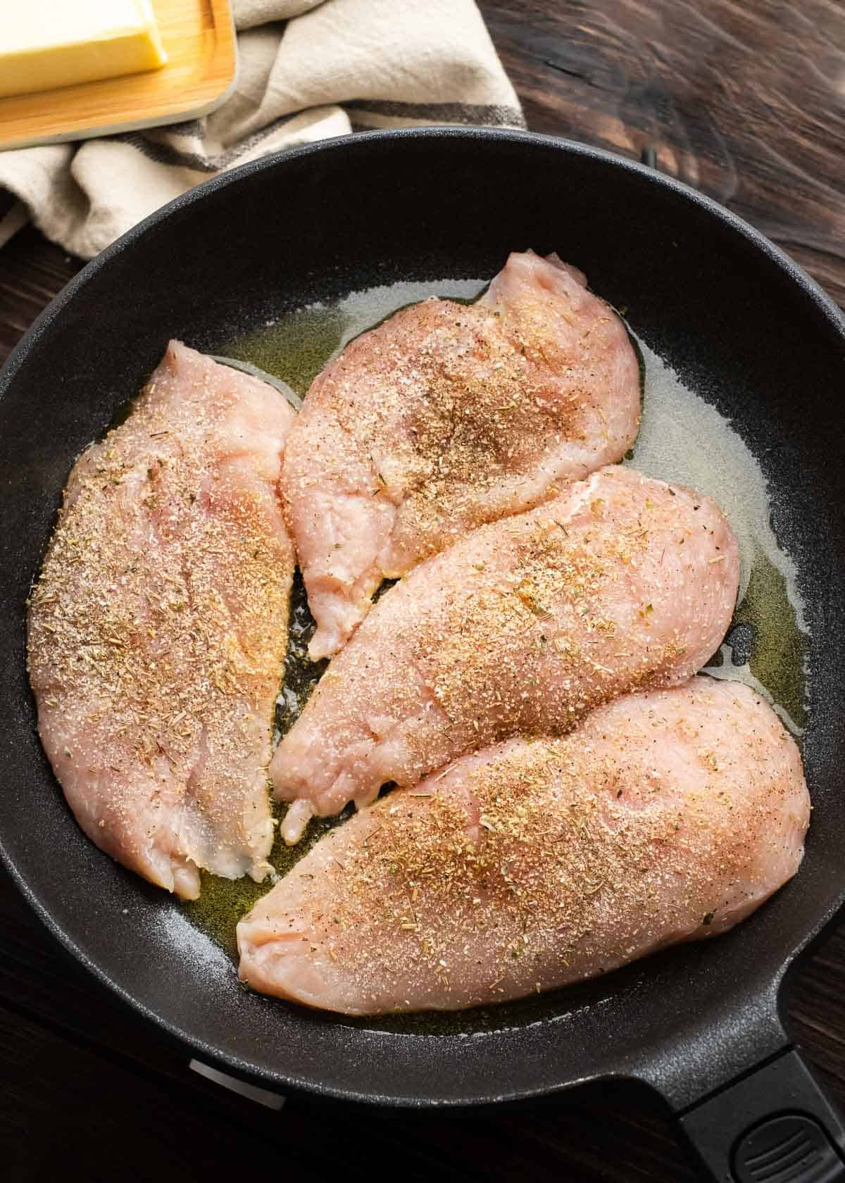 seasoned, raw chicken in a cast iron skillet