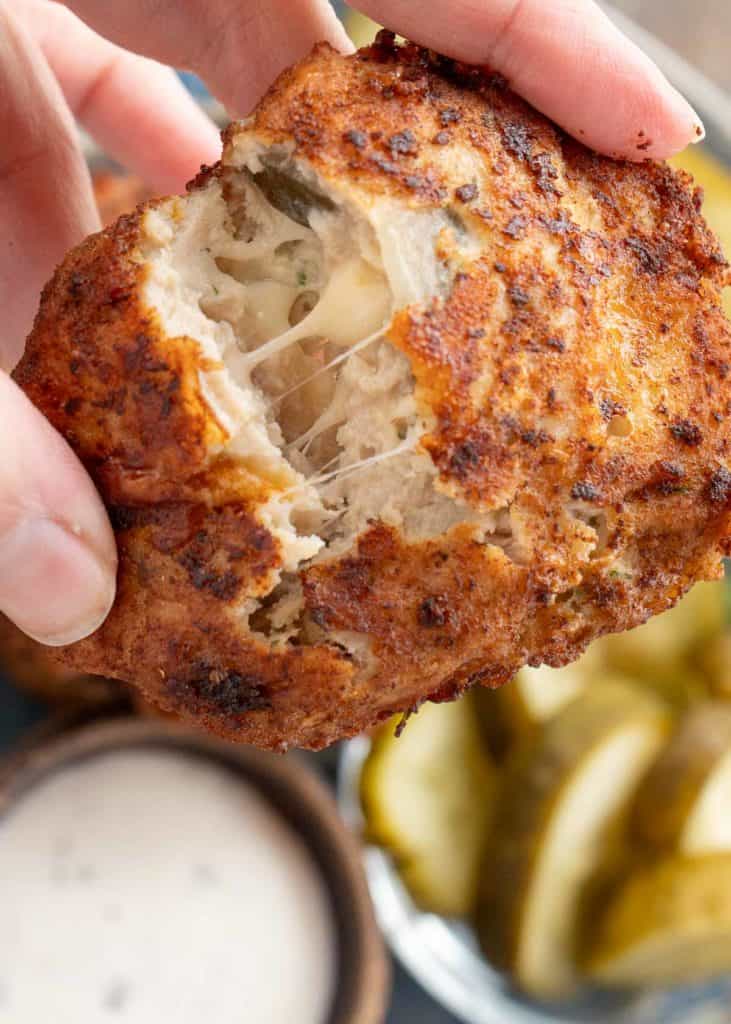two hands breaking apart a dill pickle chicken fritters to show how juicy, cheesy, and tender it is