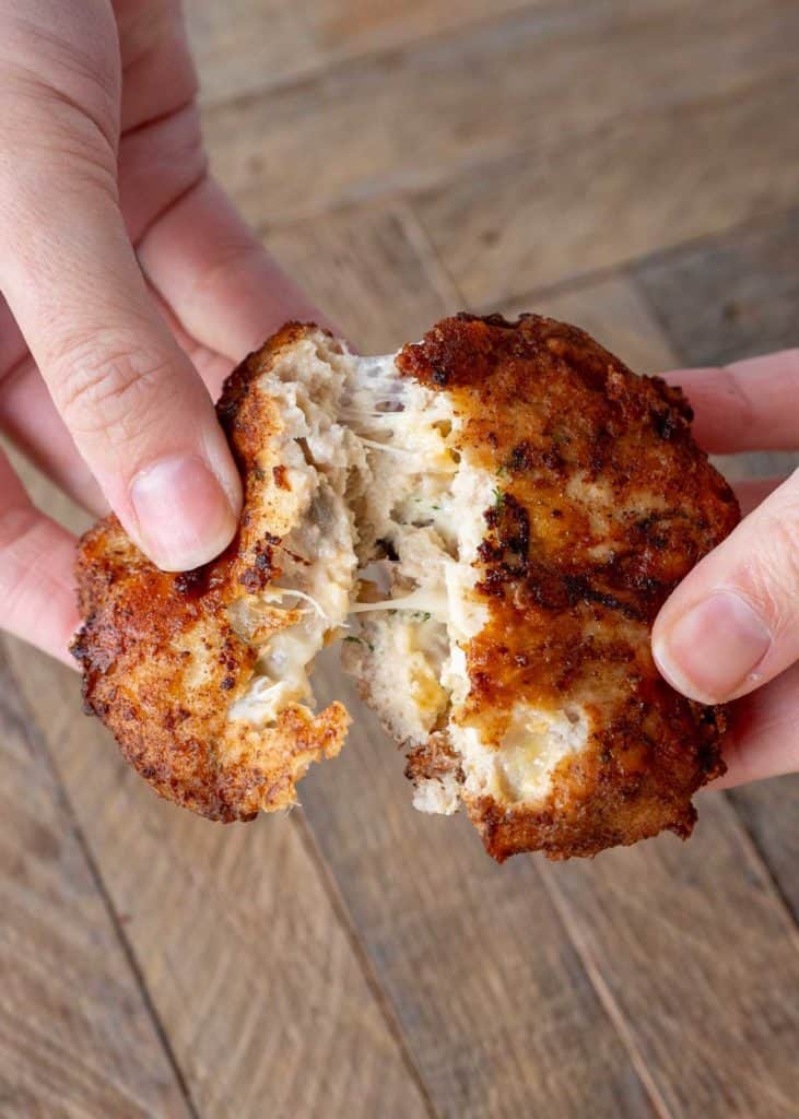 two hands holding a cheesy chicken fritter with dill pickles and juicy chicken