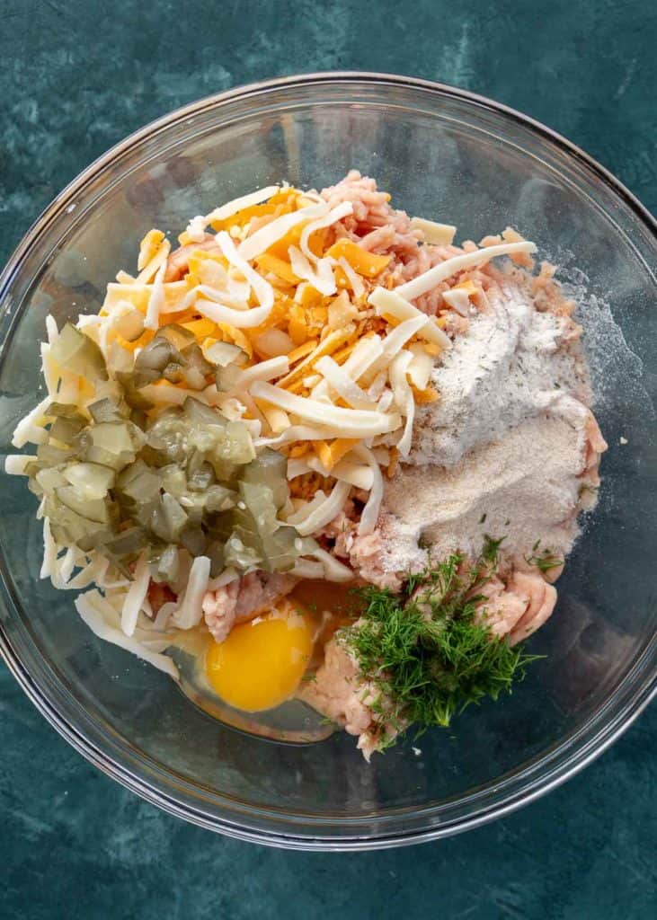 ground chicken, shredded cheese, diced dill pickles, egg, and dill in a glass bowl for chicken fritters