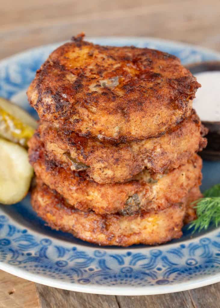 a stack of four dill pickle chicken fritters with a side of ranch and pickles on a plate