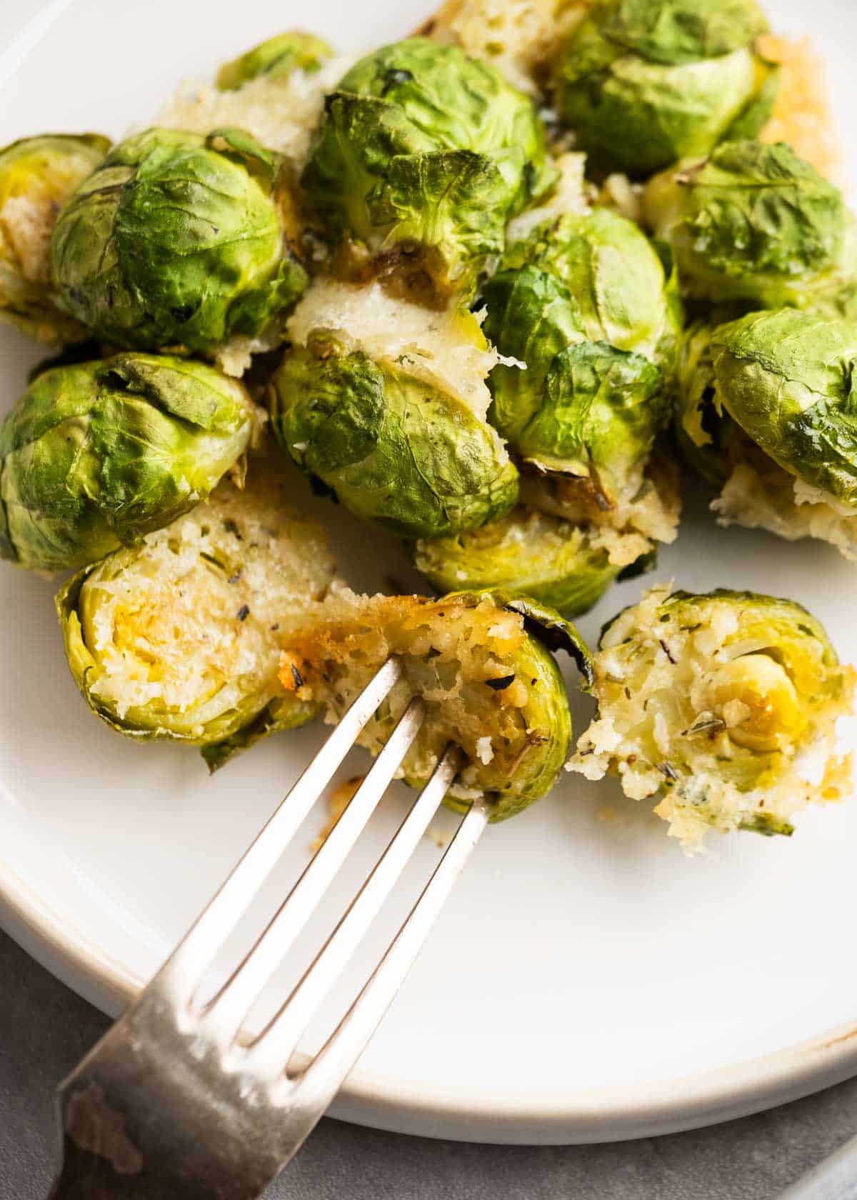 close up image of parmesan brussels sprouts and fork on a white plate