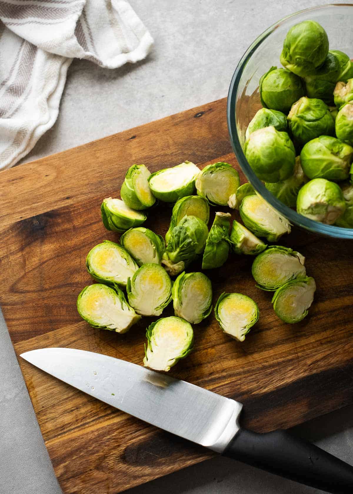 brussels sprouts being sliced in half on a wooden cutting board