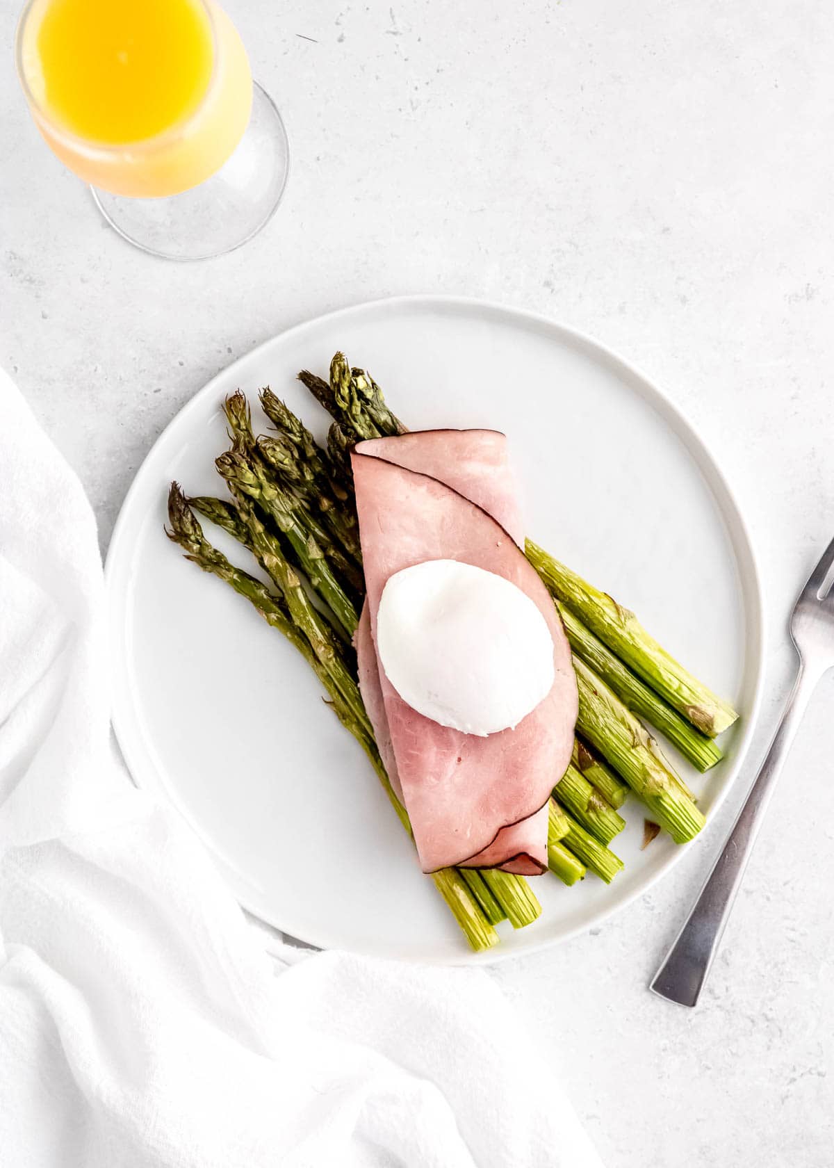 overhead image of asparagus eggs benedict being assembled on a white plate 