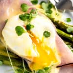close up image of a sliced eggs benedict with asparagus on a white plate