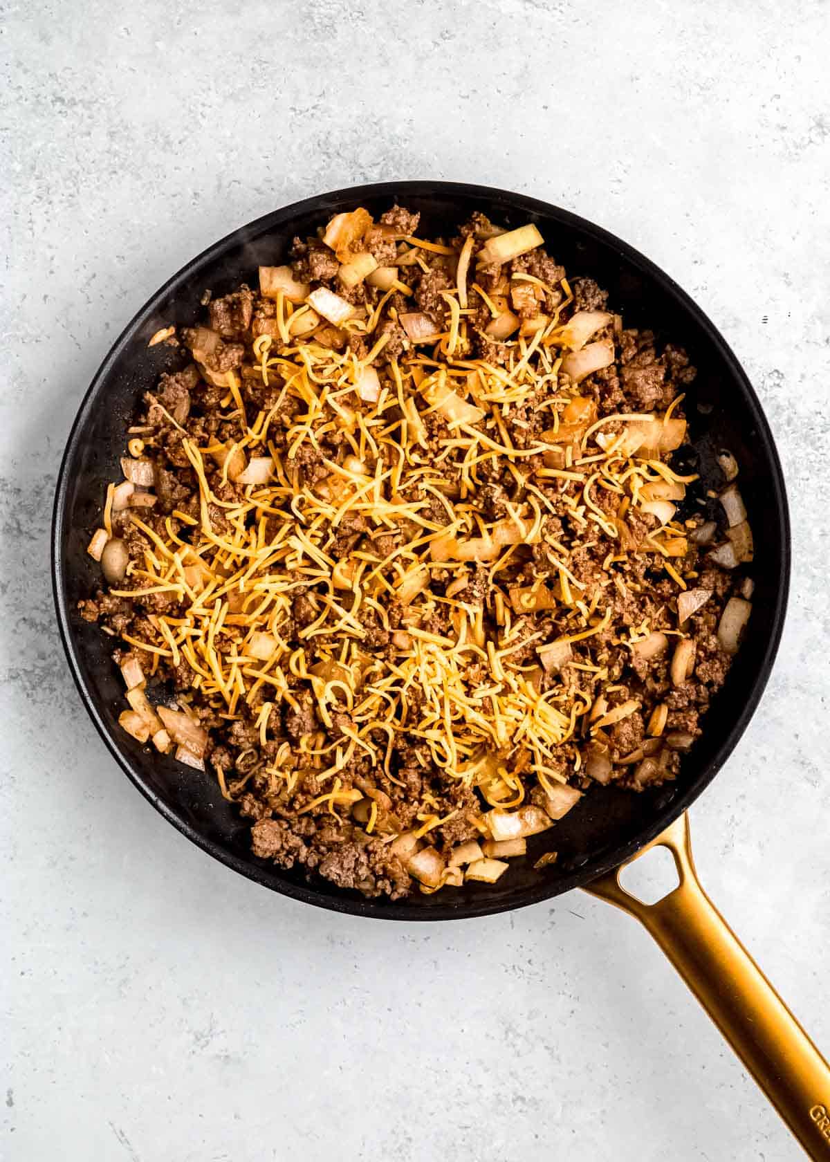 browned beef, onion, and cheese in a black skillet