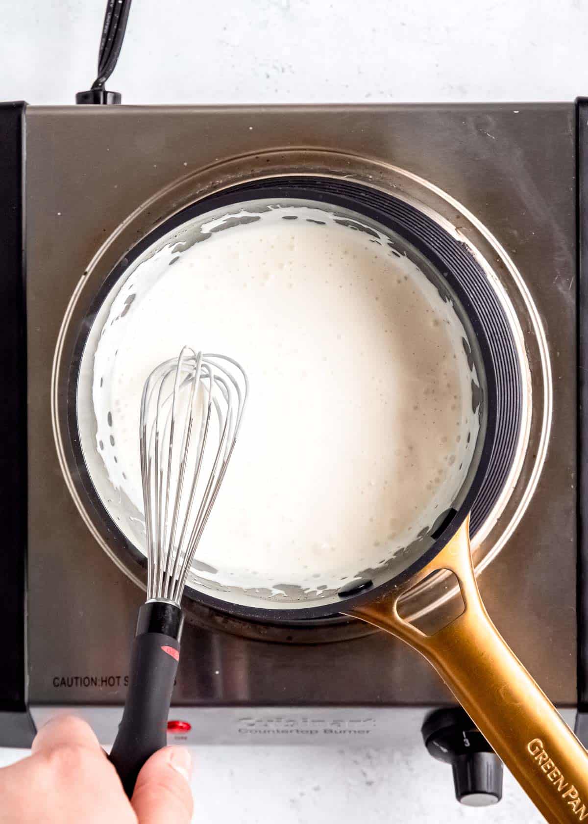 overhead image of heavy cream and cheese cheese whisked in a silver pot