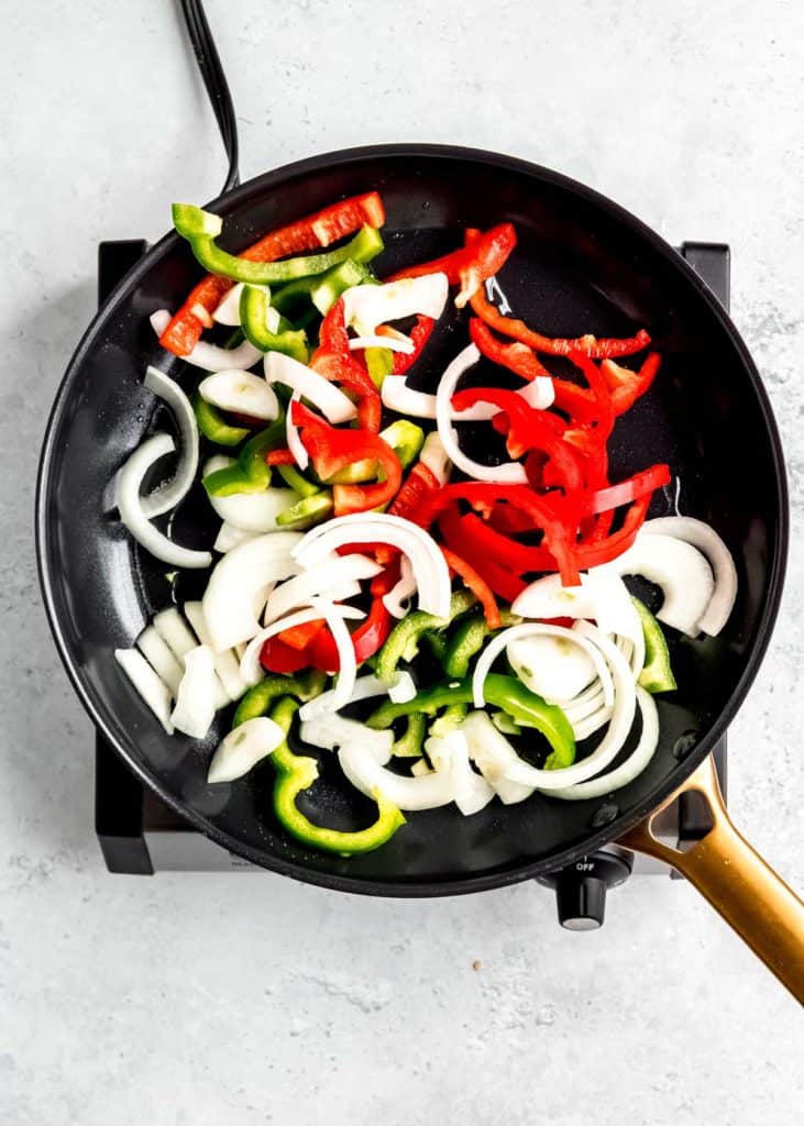 onion and peppers being sauteed in black skillet