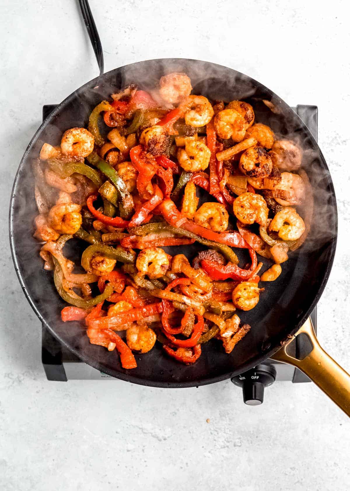 shrimp, peppers, and onions being cooked in black skillet