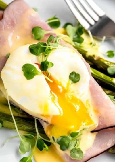 close up image of a sliced eggs benedict with asparagus on a white plate