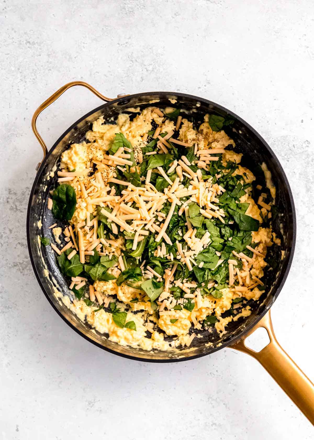 cheese, spinach, and seasonings being added to scrambled eggs