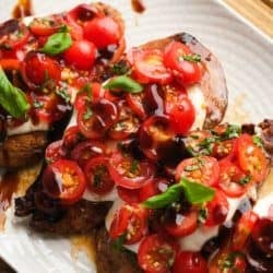 overhead image of bruschetta being added to chicken breasts on white plate