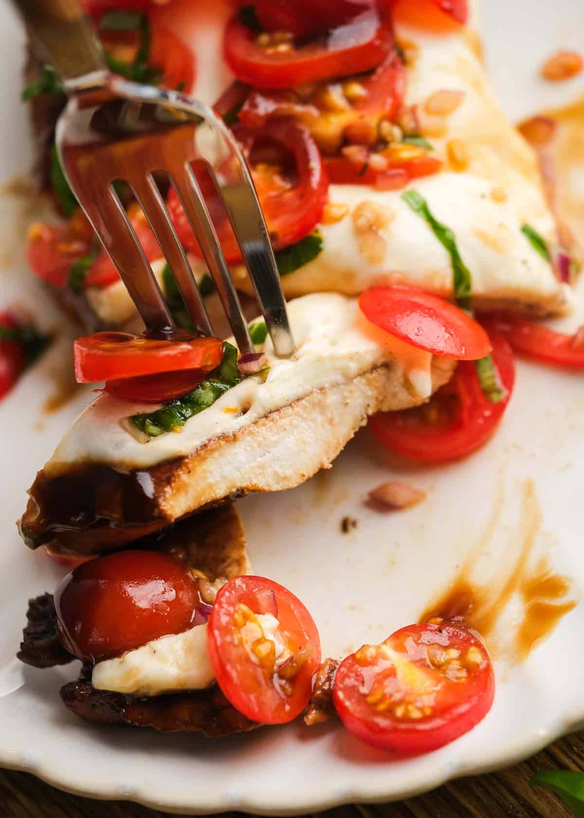 one slice of bruschetta chicken being removed from chicken breast on white plate