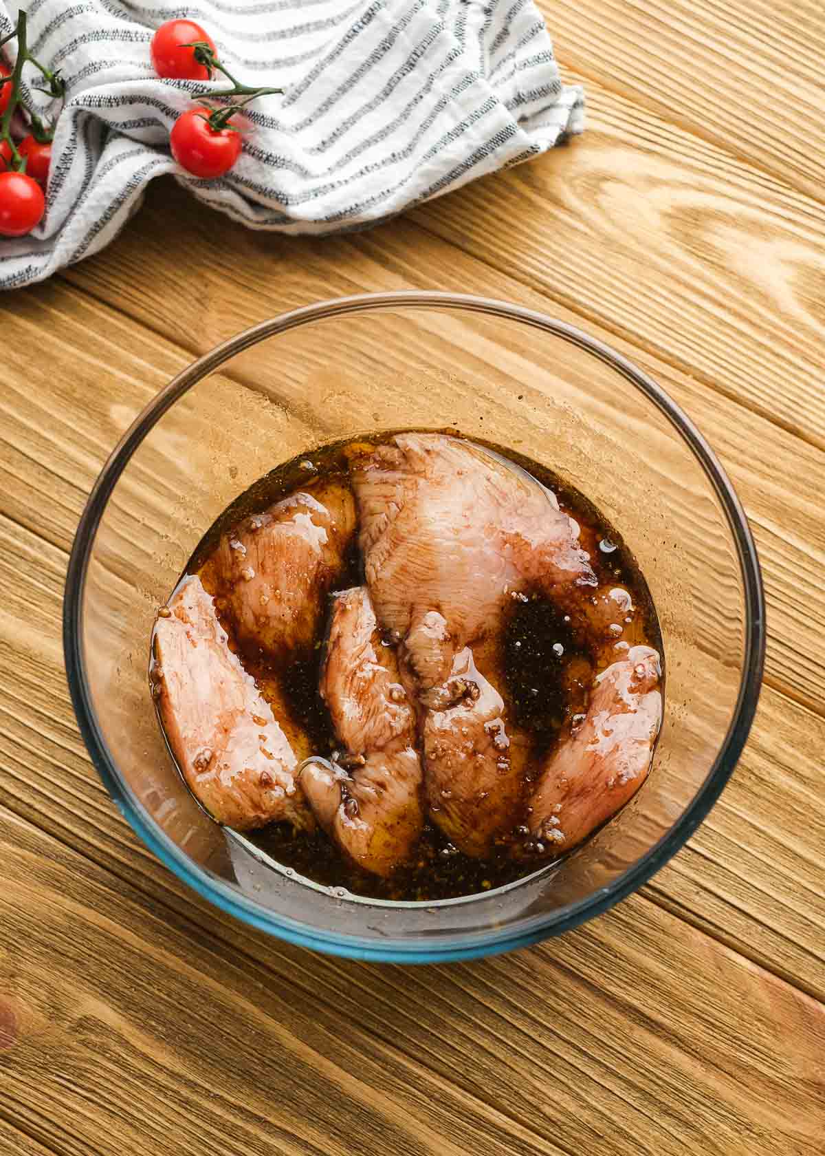 chicken marinating in a clear mixing bowl on a wooden table