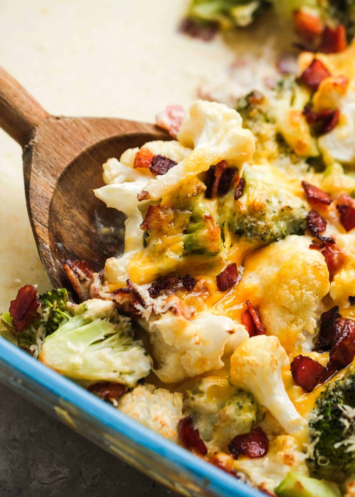 a wooden spoon scooping up a serving of cheesy broccoli cauliflower casserole