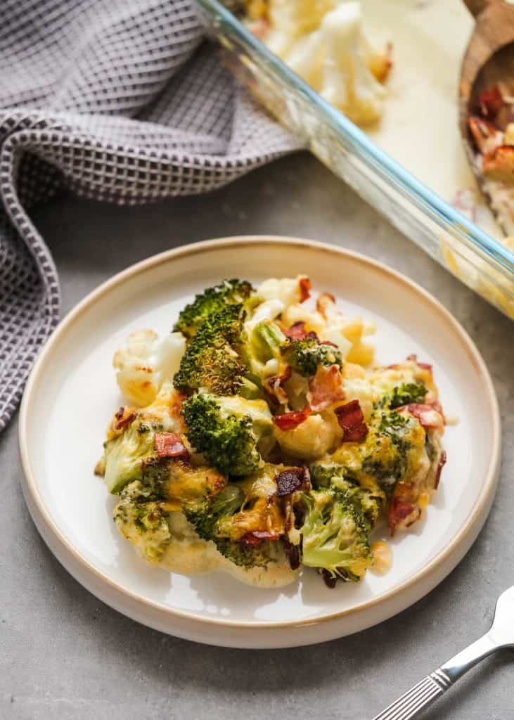 broccoli cauliflower casserole on a plate with utensils and cloth napkin in the background.