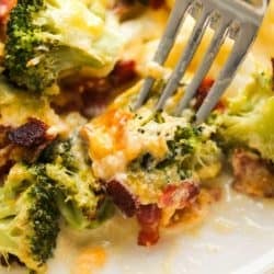 closeup photo of fork picking up a cheesy bite of broccoli cauliflower casserole on a white plate