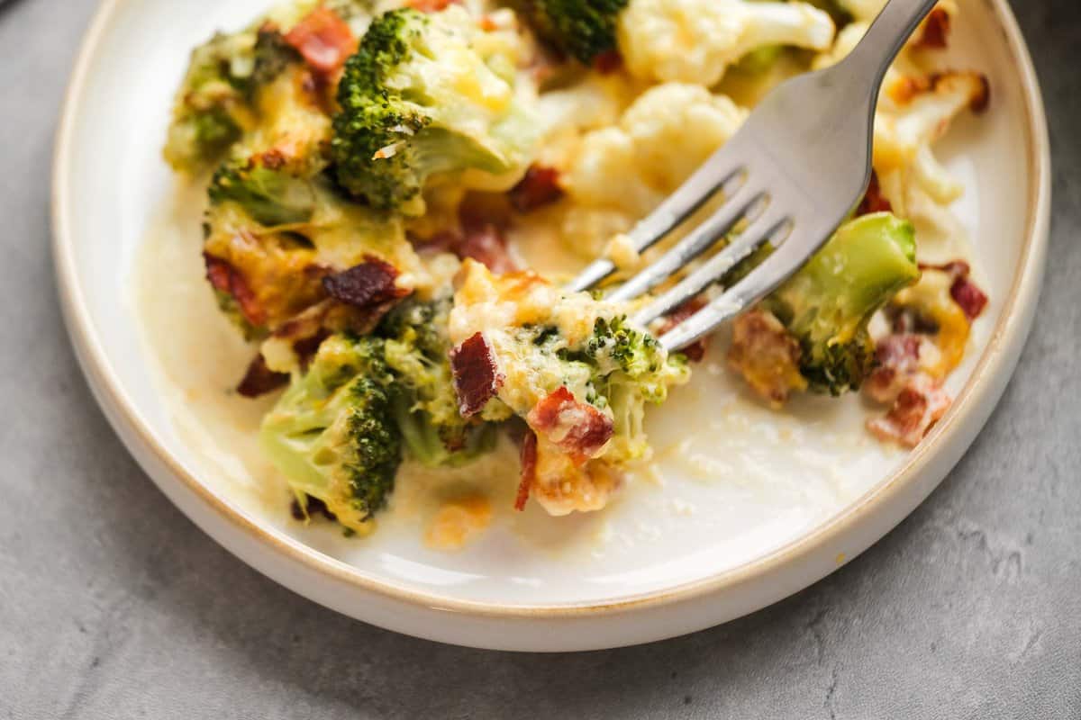 landscape closeup photo of a fork grabbing a bite of keto broccoli cauliflower casserole on a white plate