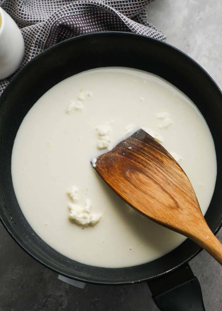 heavy cream, almond milk, and cream cheese being stirred by a wooden spoon in a skillet