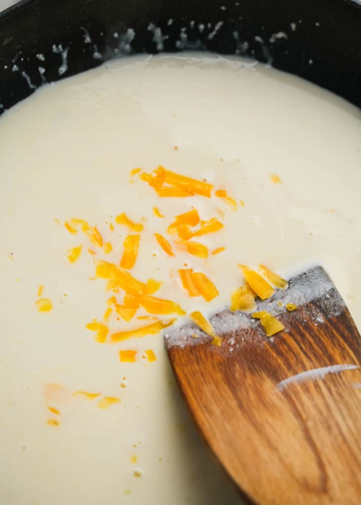 shredded cheese being stirred into a cream mixture in a skillet