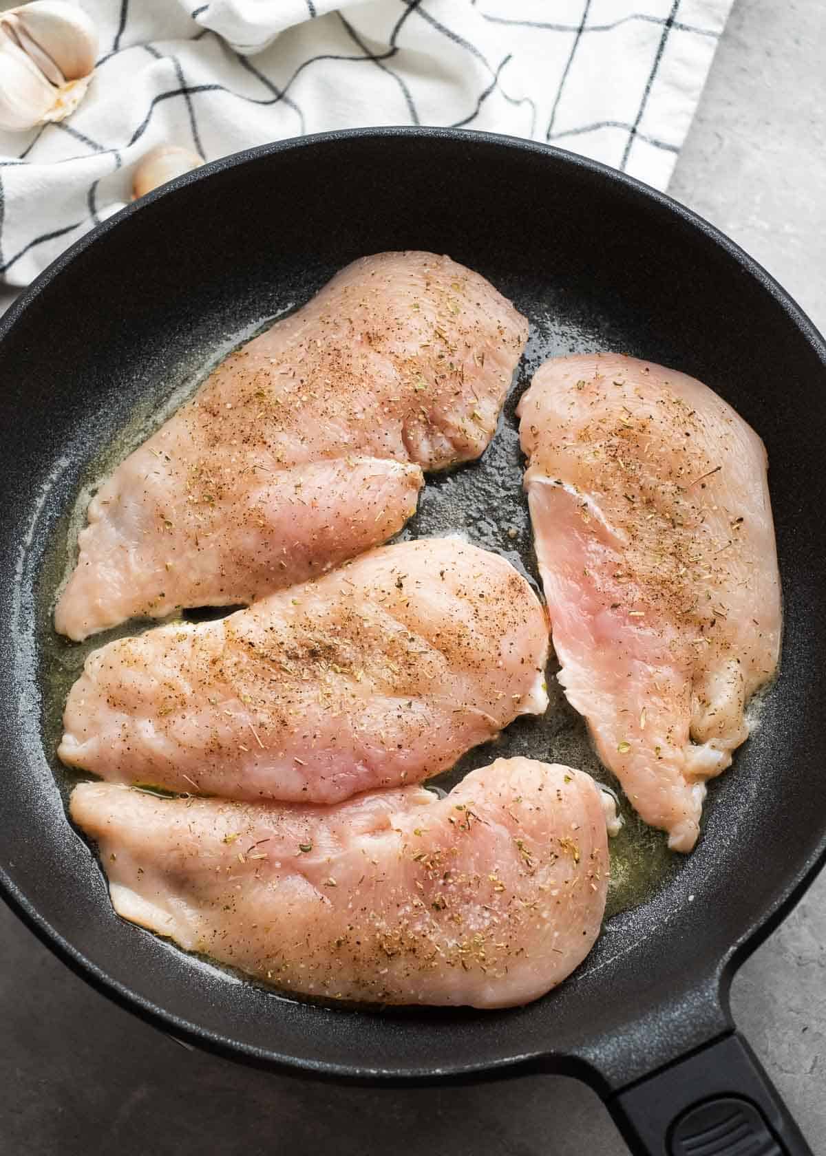 overhead image of raw chicken breasts in cast iron skillet