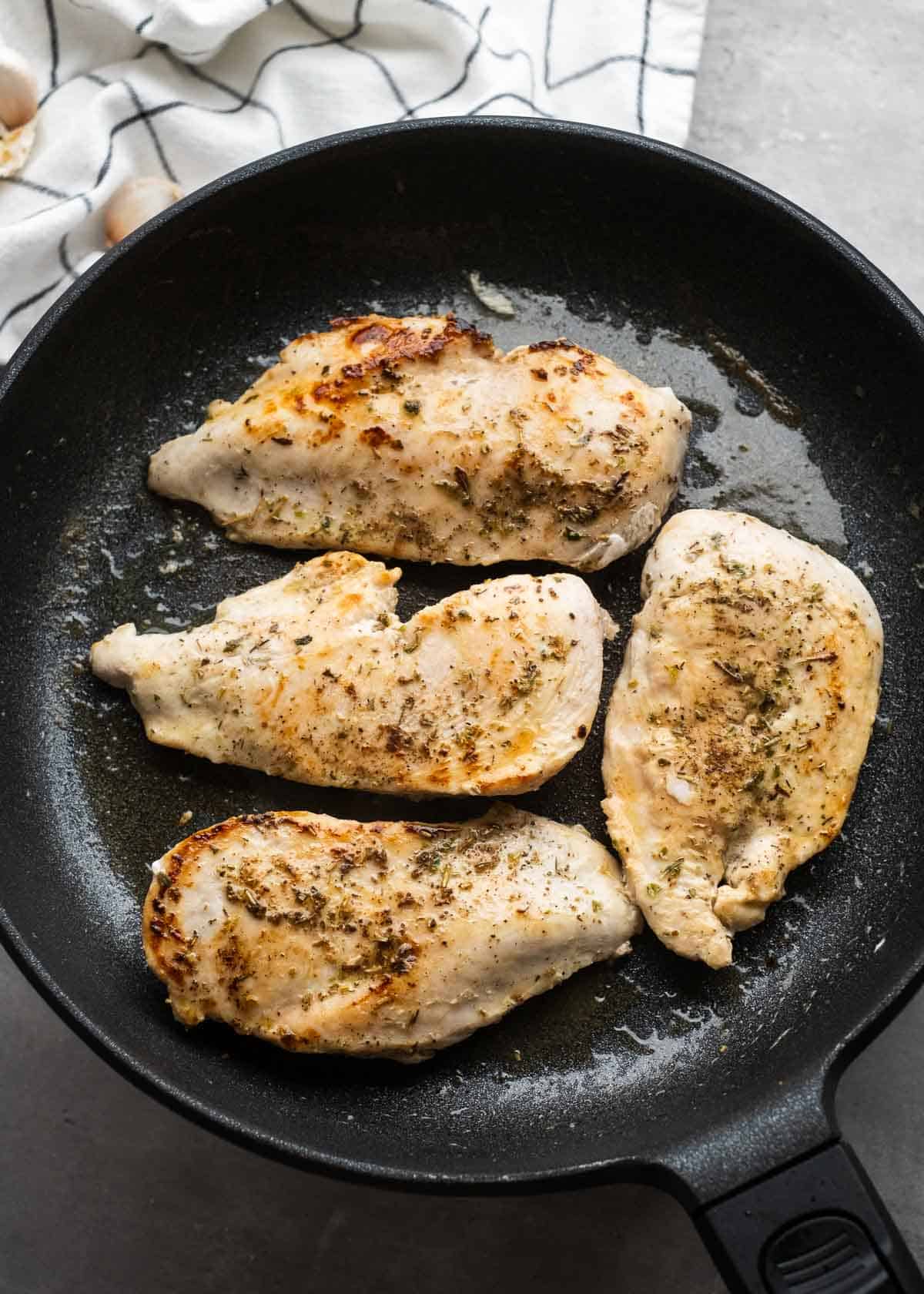 overhead image of cooked chicken breasts in cast iron skillet