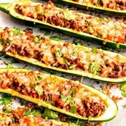 a baking sheet lined with parchment paper, topped with enchilada stuffed zucchini boats covered in melty cheese and fresh cilantro