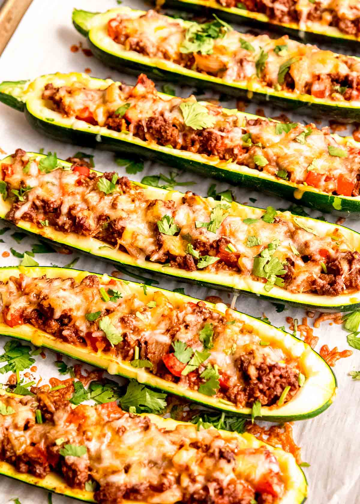 a baking sheet lined with parchment paper, topped with enchilada stuffed zucchini boats covered in melty cheese and fresh cilantro