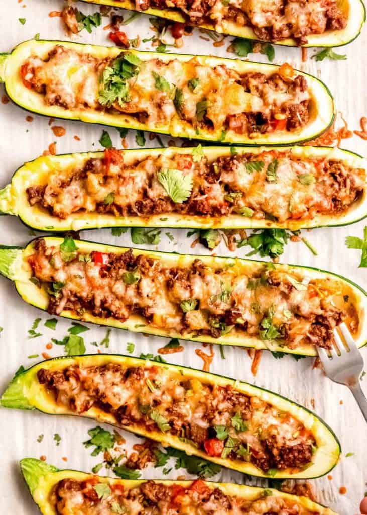 a fork pulling at the beef enchilada filling in a zucchini boat on a pan full of many boats