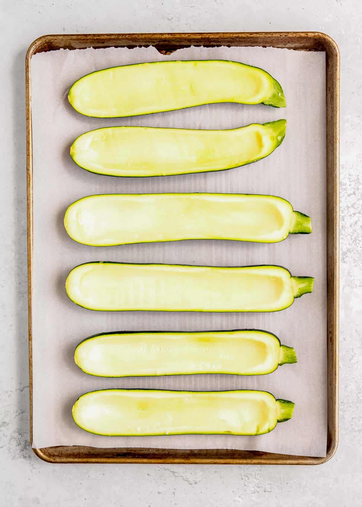 six hollowed-out zucchini halves on a parchment-paper-lined baking pan