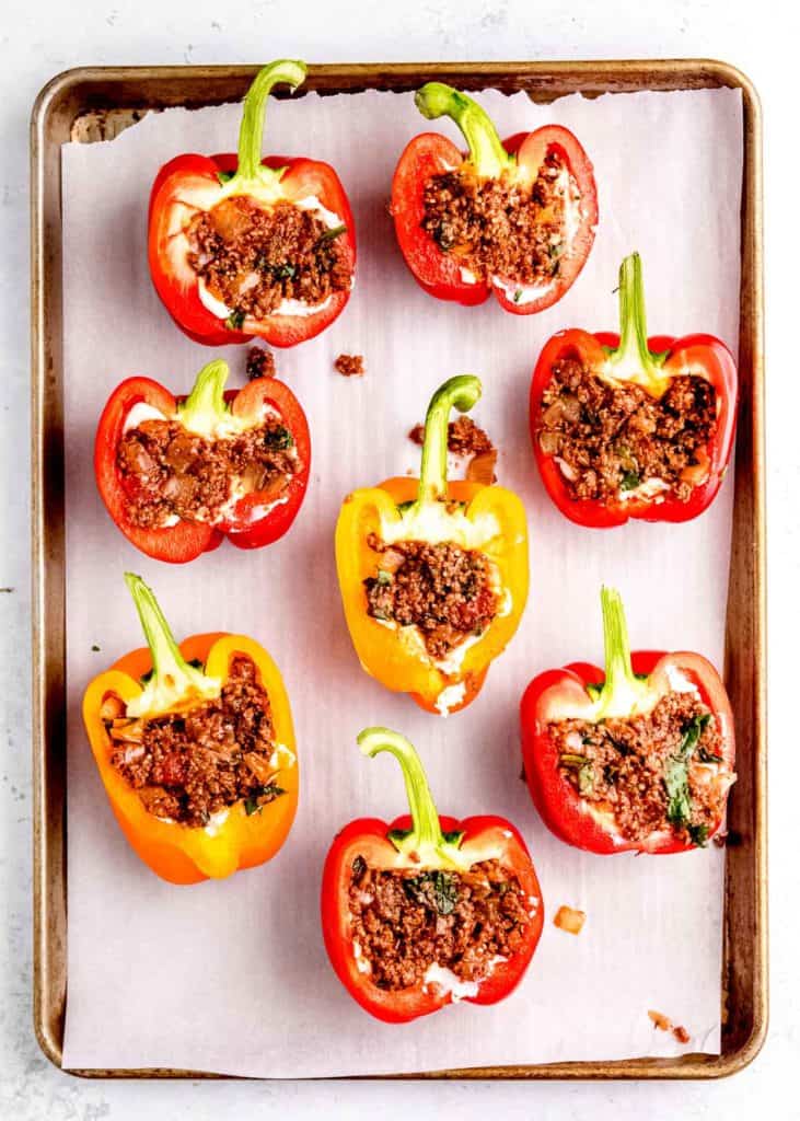 meat being added to stuffed peppers on baking sheet