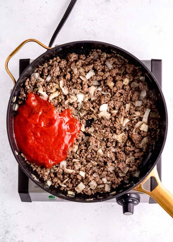 marinara being added to onion and ground beef in skillet