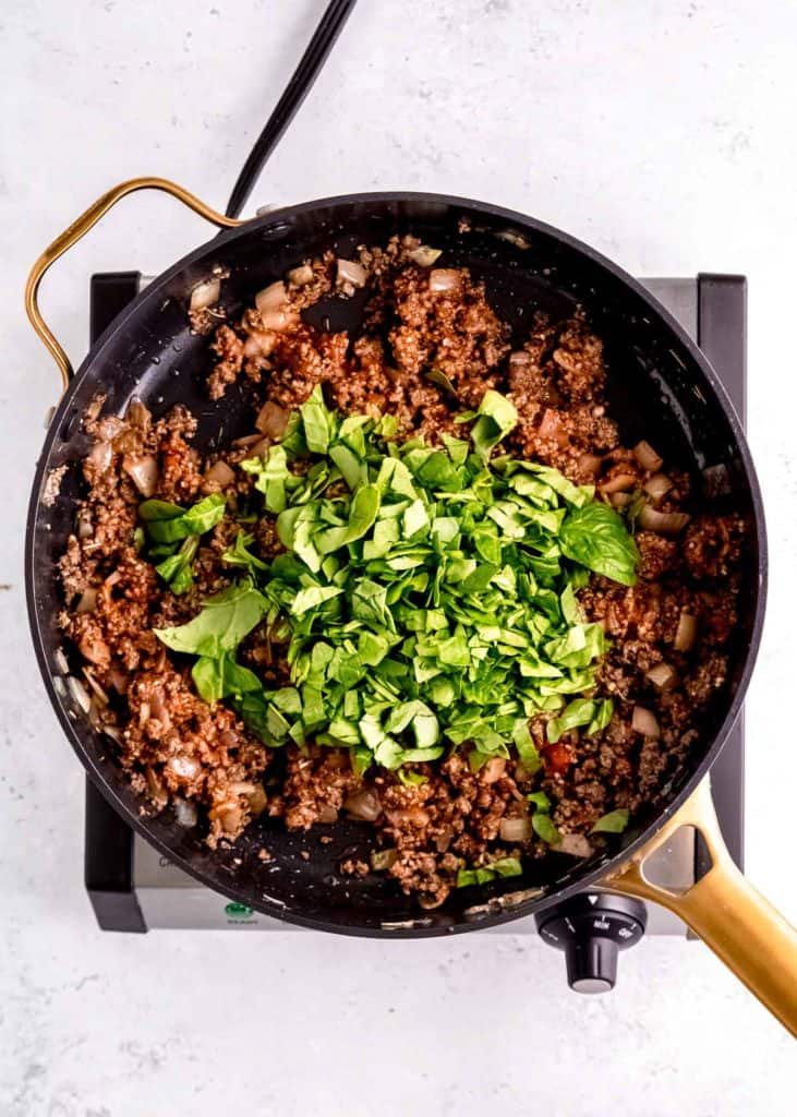 spinach being added to lasagna stuffed pepper filling