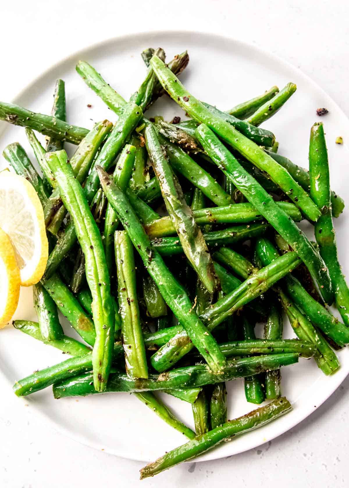overhead image of green beans and a lemon on a white plate