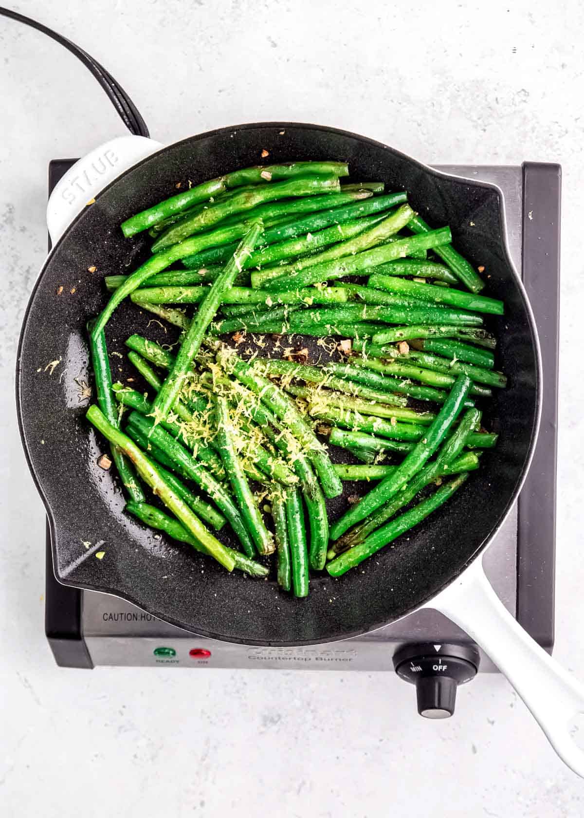 spices being added to lemon pepper green beans in skillet