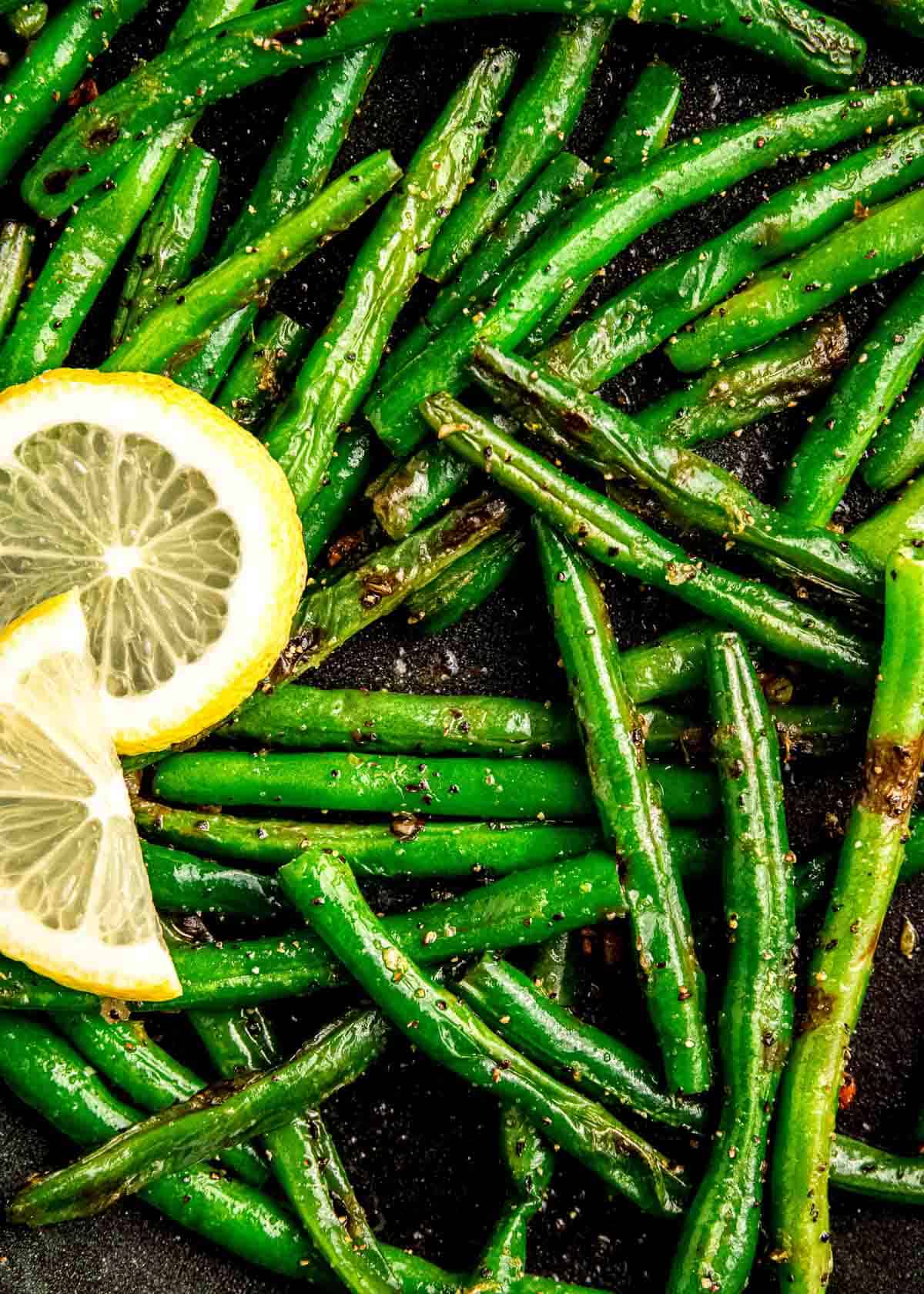 close up image of green beans and lemon slice in a skillet