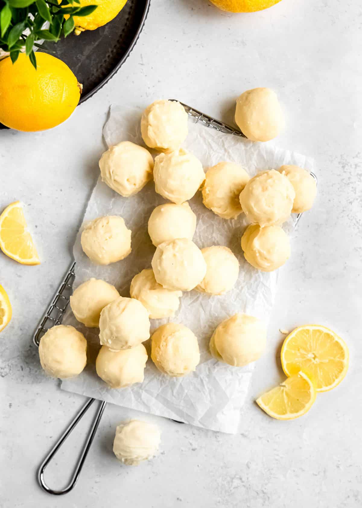 lemon truffles on a white table top after being allowed to cool with lemon slices around the truffles